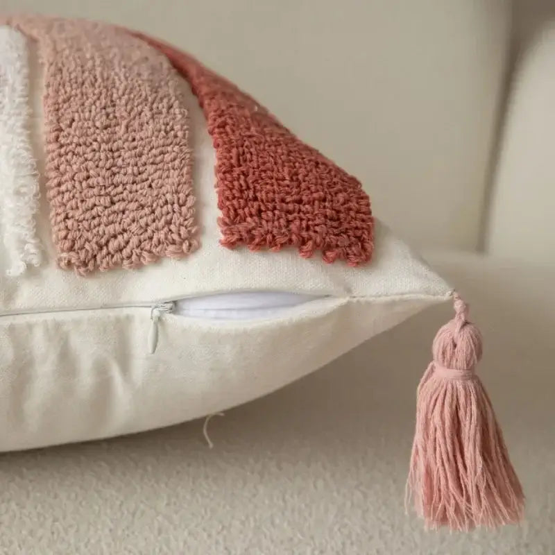 A soft cream-colored pillow cover with geometric embroidered blush pink and white yarns and a matching tassel decorbites cushion covers