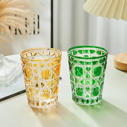 Two faceted glass tumblers in amber and emerald green feature a geometric diamond pattern heavy whiskey glass design