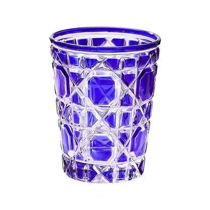 A heavy whiskey glass tumbler with a clear body, cobalt blue rim, and intricate geometric cut patterns