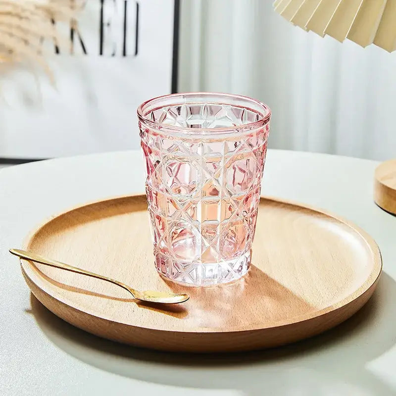 A pink faceted glass tumbler with geometric pattern on wooden tray in a heavy whiskey glass dining room set