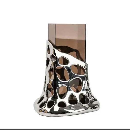 Silver metallic glass vase with sculpted irregular cutouts holding a tall amber glass for geometric acrylic decorbites living room use