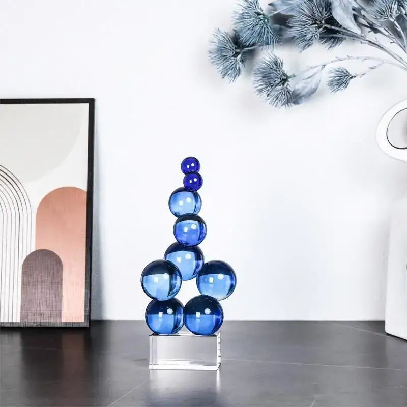 A sleek geometric crystal sculpture with stacked blue spheres on a clear acrylic base for living room decor