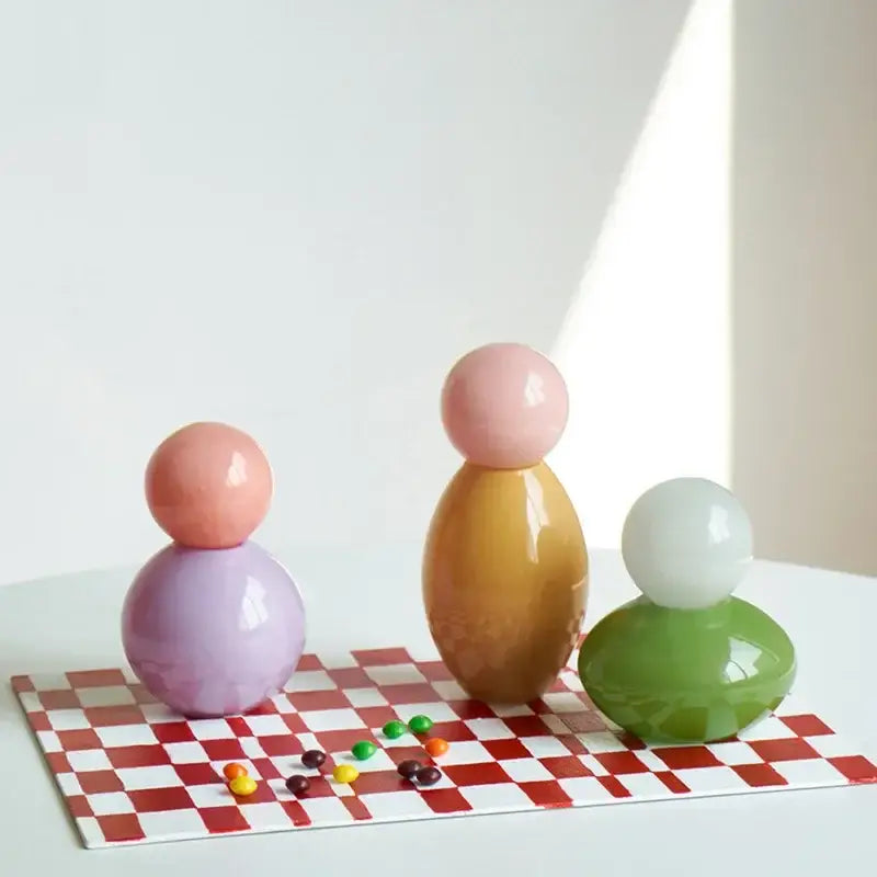 Pastel-colored glossy ceramic figurines on red and white checkered surface complement geometric sphere glass vase storage container