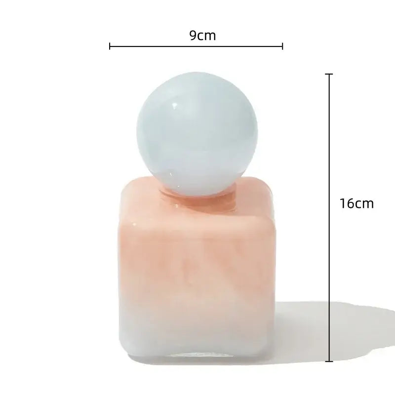 A geometric sphere glass vase with lid in peachy-pink fading to white and a pale blue spherical cap for desktop storage
