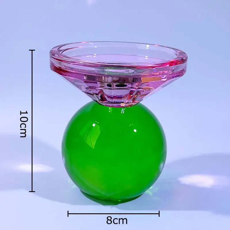 A vibrant translucent pink and green crystal candle holder with a faceted top and smooth spherical base for dining room