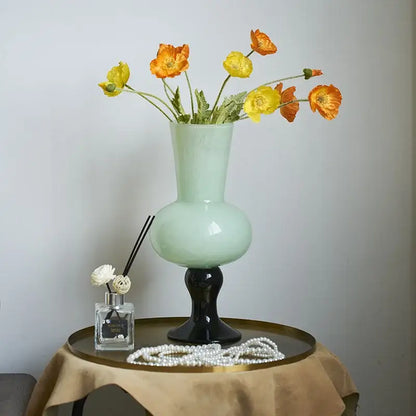 A sleek pale green ceramic vintage glass vase with black pedestal base holds vibrant orange poppies decorbites geometric vintage