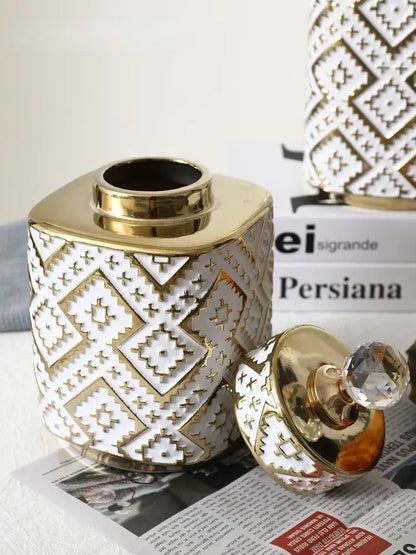 A white ceramic decorative jar with golden relief geometric patterns and a matching golden lid with crystal knob by decorbites
