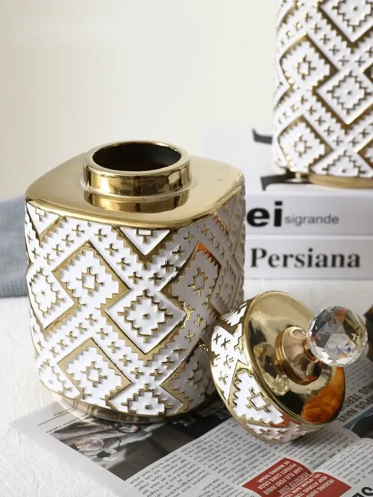 A white ceramic decorative jar with golden relief geometric patterns and a matching golden lid with crystal knob by decorbites