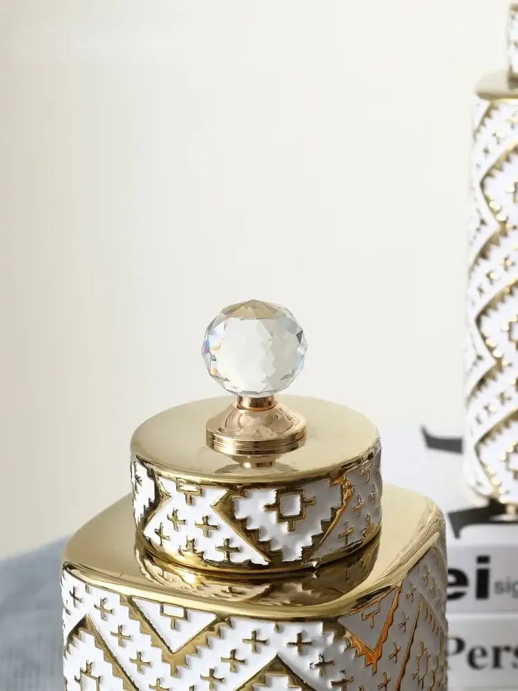 A gold and white ceramic decorative jar with geometric golden relief and a faceted crystal knob kitchen canister