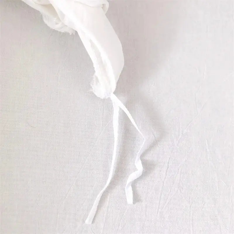 Delicate white fabric ribbon with frayed edge on geometric white quilted duvet cover set for bedroom bedding