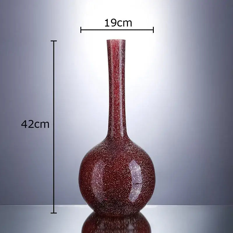 A tall slender gilded red glass vase with speckled texture and rounded base holding artificial flowers decorbites gilded red