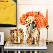 Gold-toned gilded tree branch glass vase with intricate leaf detailing holding orange hydrangeas and white berries