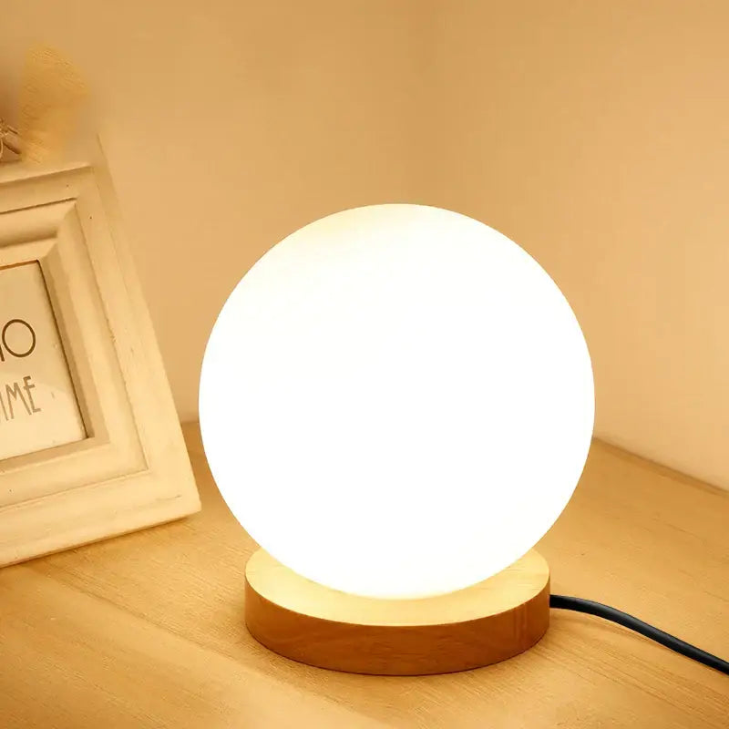 A warm glowing glass ball led table lamp with matte white finish and wooden base for bedroom night light decorbites glass ball