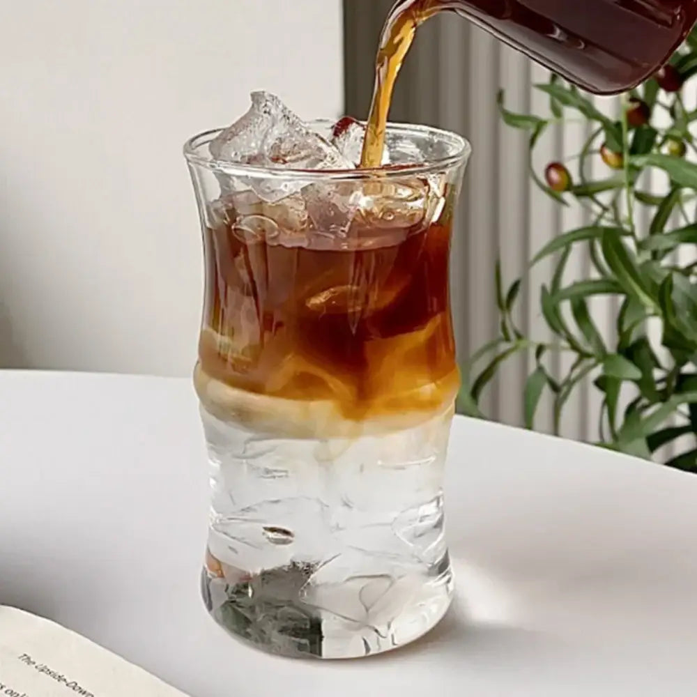 A clear glass bamboo knot mug filled with ice and layered coffee being poured into the textured cup