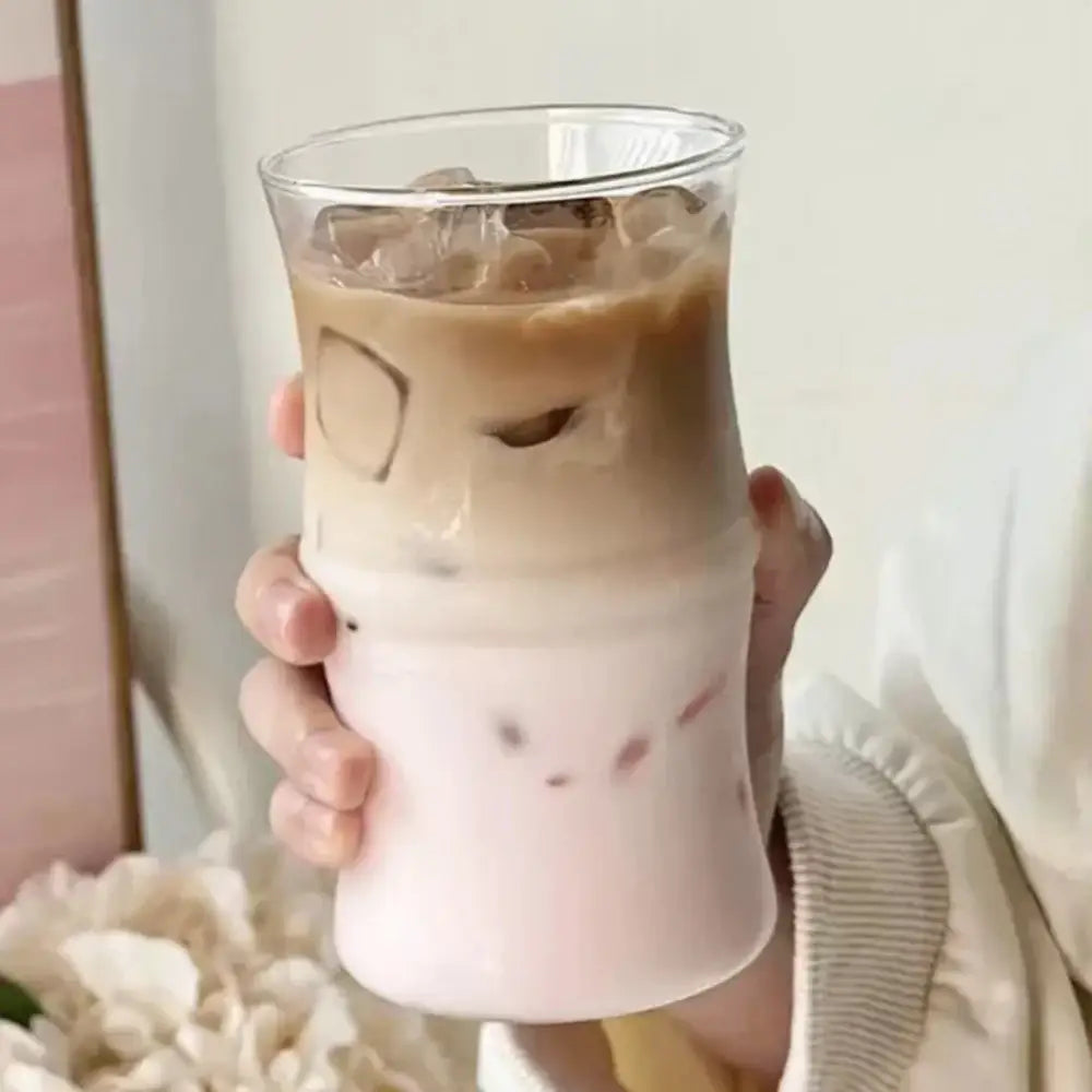 A clear glass bamboo knot mug filled with a layered iced coffee drink featuring ice cubes and pinkish milk layer