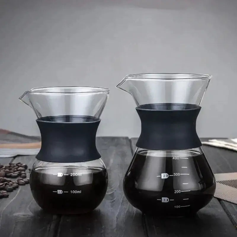 Two glass coffee pot pour-over drippers with black silicone handles and stainless steel filters filled with dark coffee