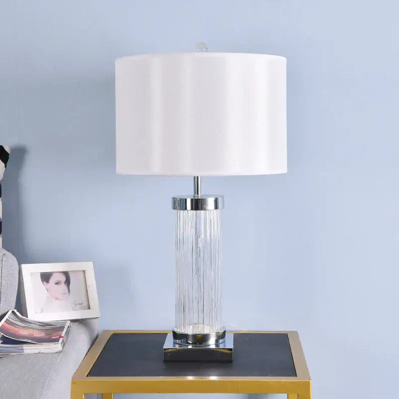Clear glass crystal cylinder table lamp with vertical ridges chrome accents and cream drum shade for bedroom use