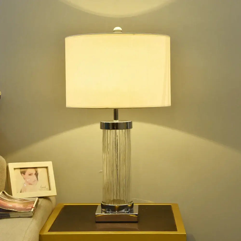 A modern glass crystal cylinder table lamp with clear ribbed glass base and cream rectangular shade for bedroom use