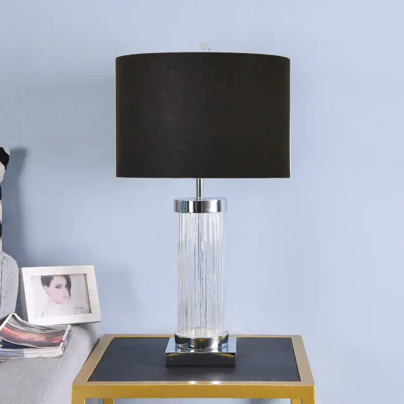 A sleek table lamp with black fabric shade, clear glass crystal cylinder body, and polished chrome accents for bedroom