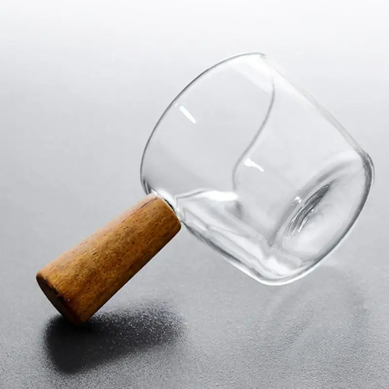 Glass espresso measuring cup with clear glass body and smooth rounded light brown wood handle for kitchen use