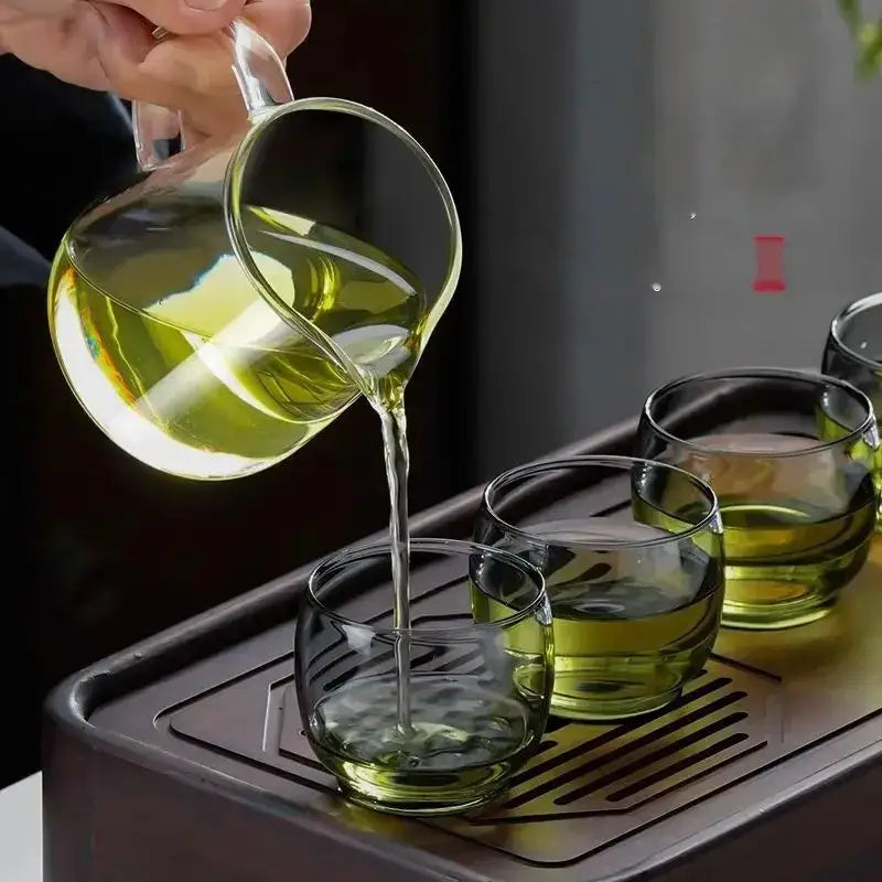 Clear glass gaiwan cup set with wood ring pouring green tea into matching glass gaiwan cups in dining room setting