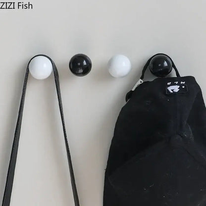 Set of four glossy black and white ceramic wall hooks with smooth finishes for a minimalist hook clothing rack