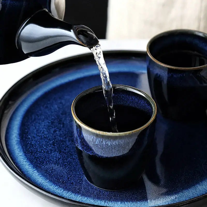 Glossy blue ceramic tea kettle set with bamboo handle pouring liquid into matching cup on a ceramic tray decorbites blue ceramic