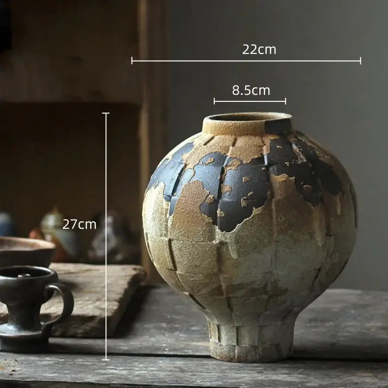 A rustic handcrafted green ceramic spherical vase with an earthy beige glaze and cracked black patches for living room decor