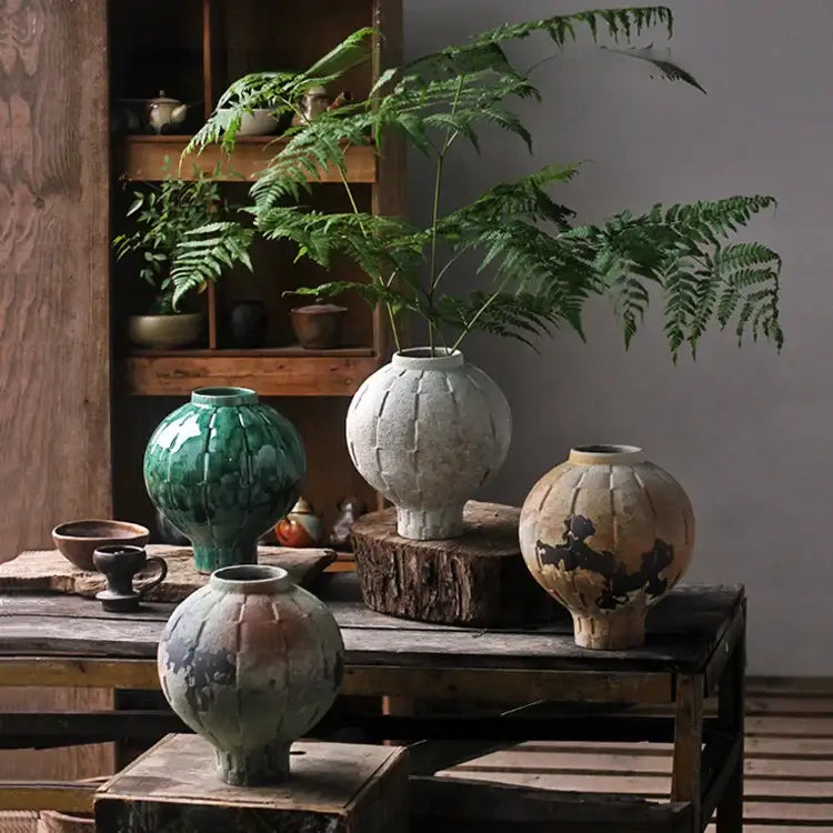 A rustic green ceramic spherical vase with a rounded body and subtle vertical ridges for living room decor