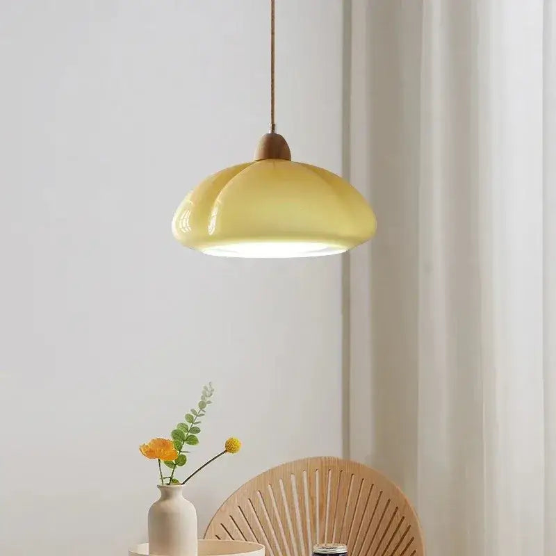 A soft yellow glossy ceramic pendant light with wooden top and cord for bedroom lighting in a pumpkin chandelier style