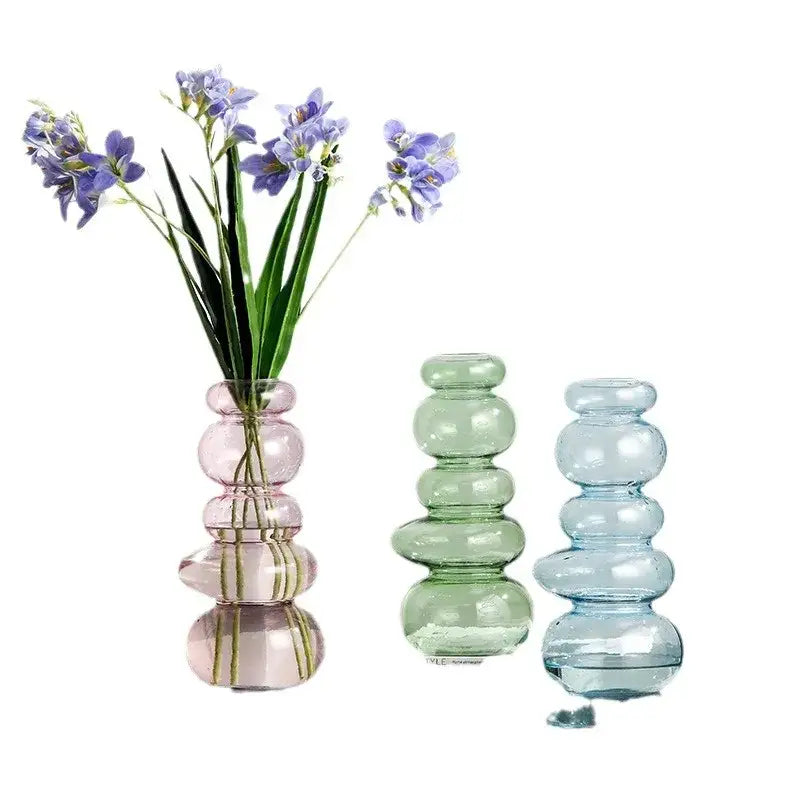A translucent pink glass pebble stack floral vase with stacked rounded design holding delicate purple flowers
