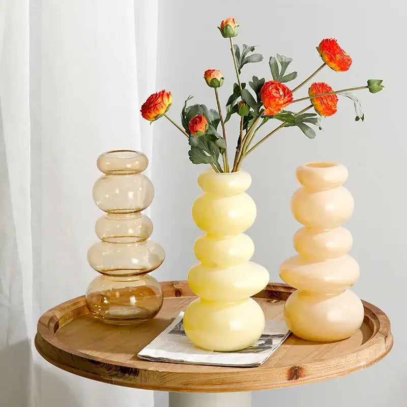 Glossy pastel pink pebble stack floral arrangement with three stacked rounded glass vases in amber and cream hues