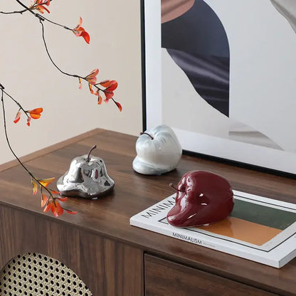 A glossy red abstract melting apple ceramic sculpture with a small stem sitting on a magazine for living room decorbites decor