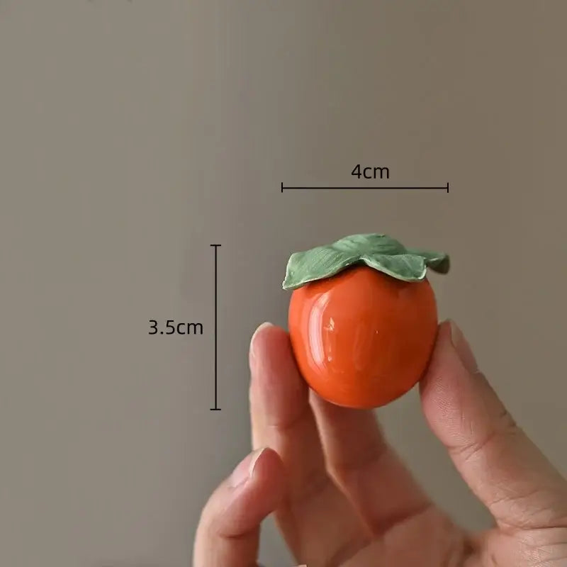 Glossy orange ceramic persimmon fruit sculpture with green leaf details, 4cm wide, ideal for sculpture tea caddy decor