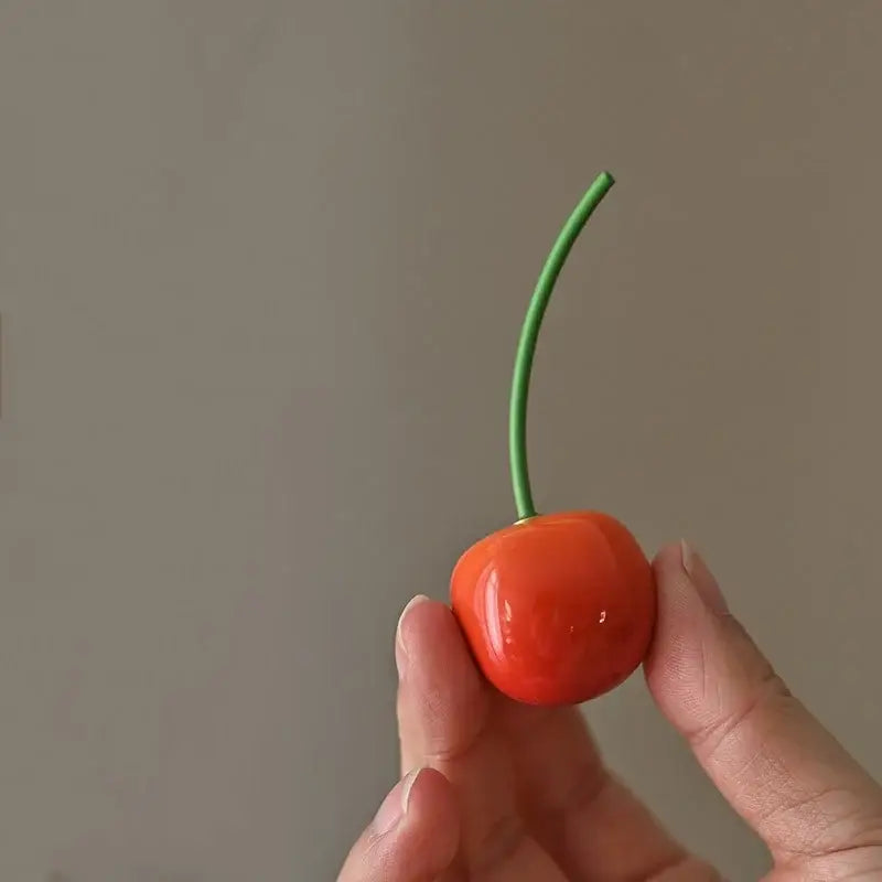 Glossy orange ceramic fruit sculpture tea caddy shaped like a cherry with a slender green stem held between fingers