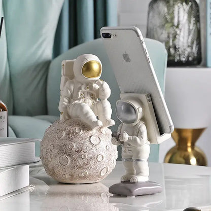 Glossy white and gold astronaut phone holder figurine seated on textured moon surface for bedroom decor