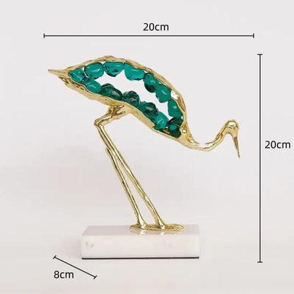 Gold and emerald crystal crane sculpture with golden body and teal gemstone details on white marble base for decor