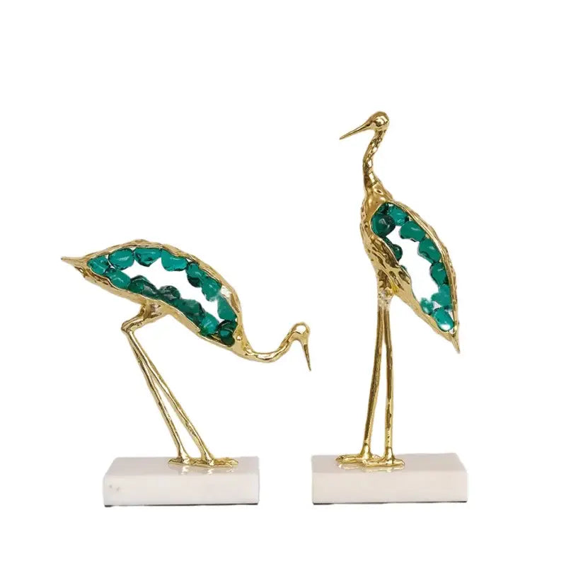 Two elegant gold-toned crystal crane sculptures with teal gemstones on white marble bases for living room decor