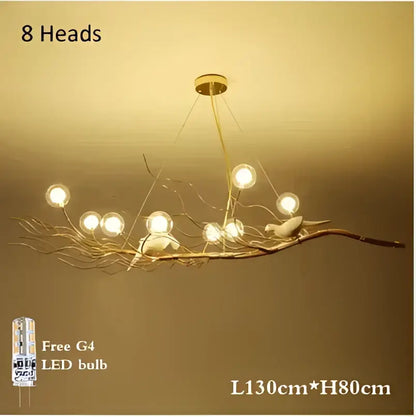 A gold and white iron branch led pendant chandelier with eight glowing bulbs and bird figurines for dining room use