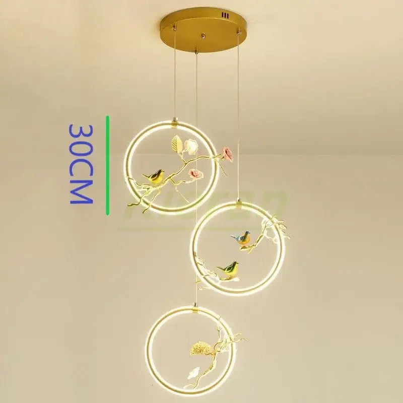 Gold-toned decorbites bird led chandelier with three hanging rings featuring floral designs for dining room lighting