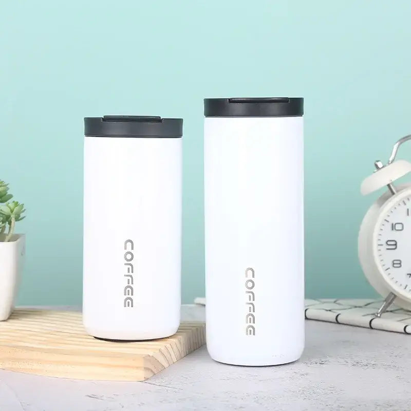 Two white decorbites insulated espresso cup tumblers with black lids and silver coffee lettering for travel use