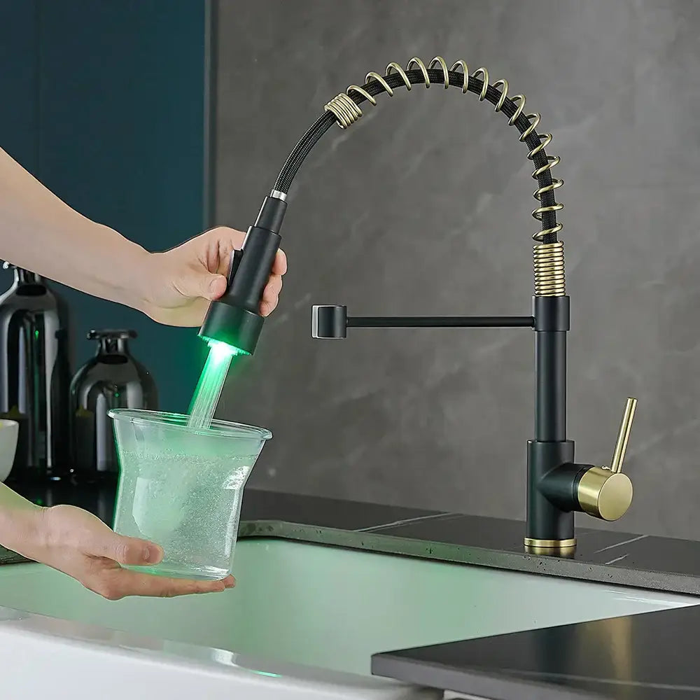 Black and gold decorbites brass spring kitchen faucet with flexible coiled brass spring spout emitting green light flowing into glass