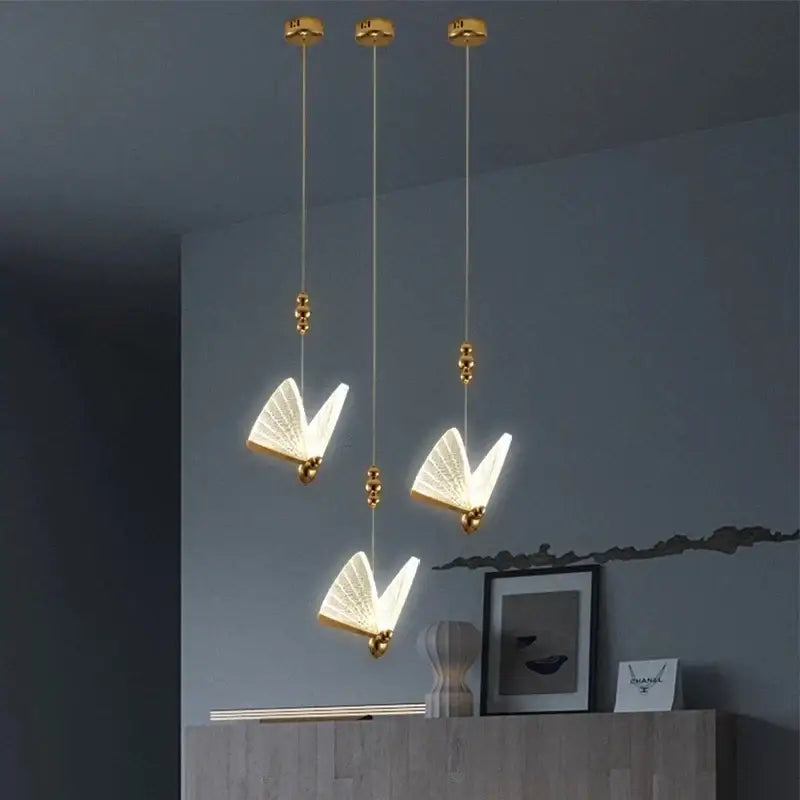 Gold butterfly pendant light with acrylic elements features translucent illuminated wings as a ceiling light source