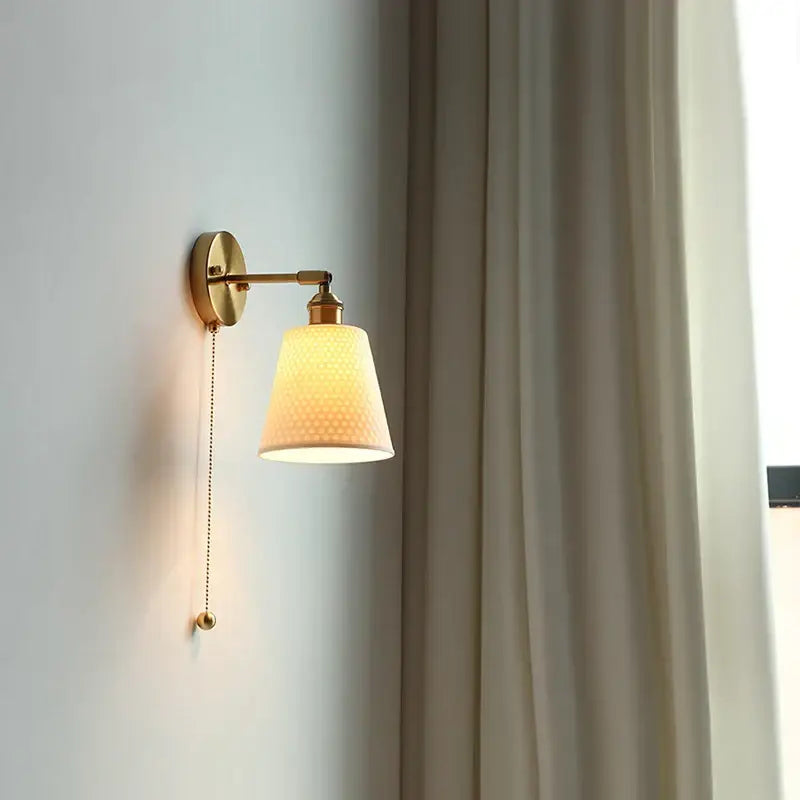 Brass-finished Decorbites ceramic led wall sconce with cream ribbed fabric shade and pull-chain switch for bedroom decor