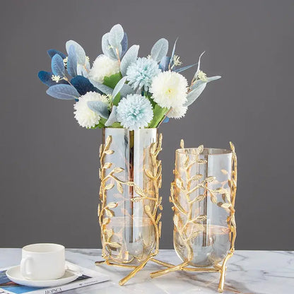 A tall clear glass vase with a gold leaf patterned metal frame and stand for coral crystal tree decor