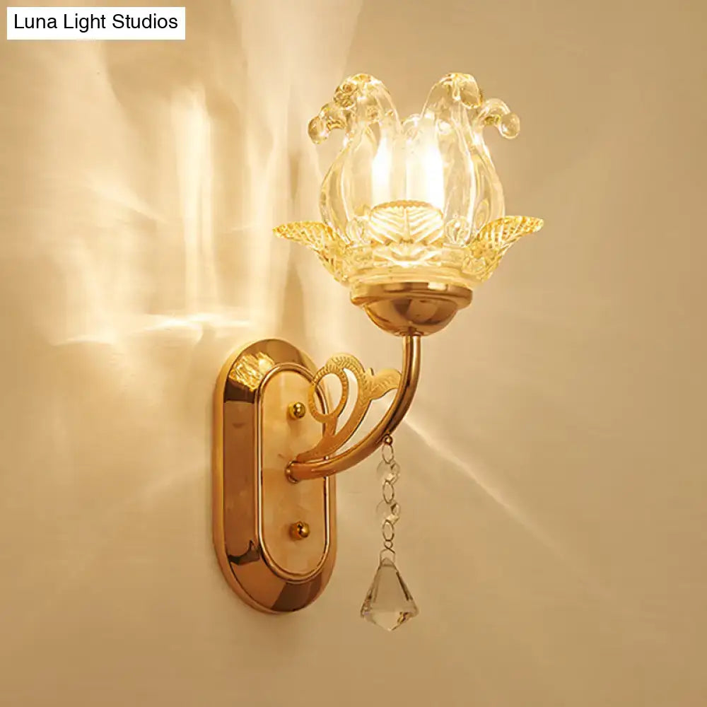 Gold-toned wall lamp with clear glass lotus-shaped shade and dangling crystal teardrop highlighting simplicity blossom fixture width