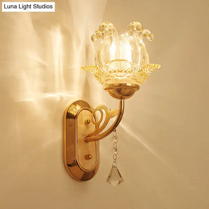 Gold-toned wall lamp with clear glass lotus-shaped shade and dangling crystal teardrop highlighting simplicity blossom fixture width