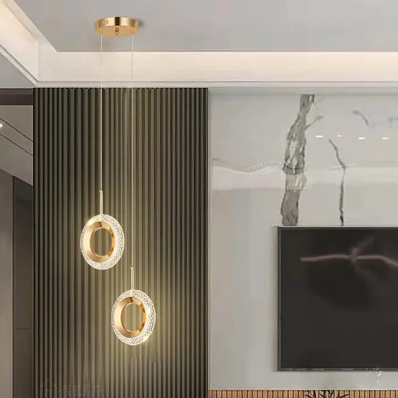 Two modern gold-toned led pendant lights with crystal-encrusted rings hang as a luxury dining room chandelier