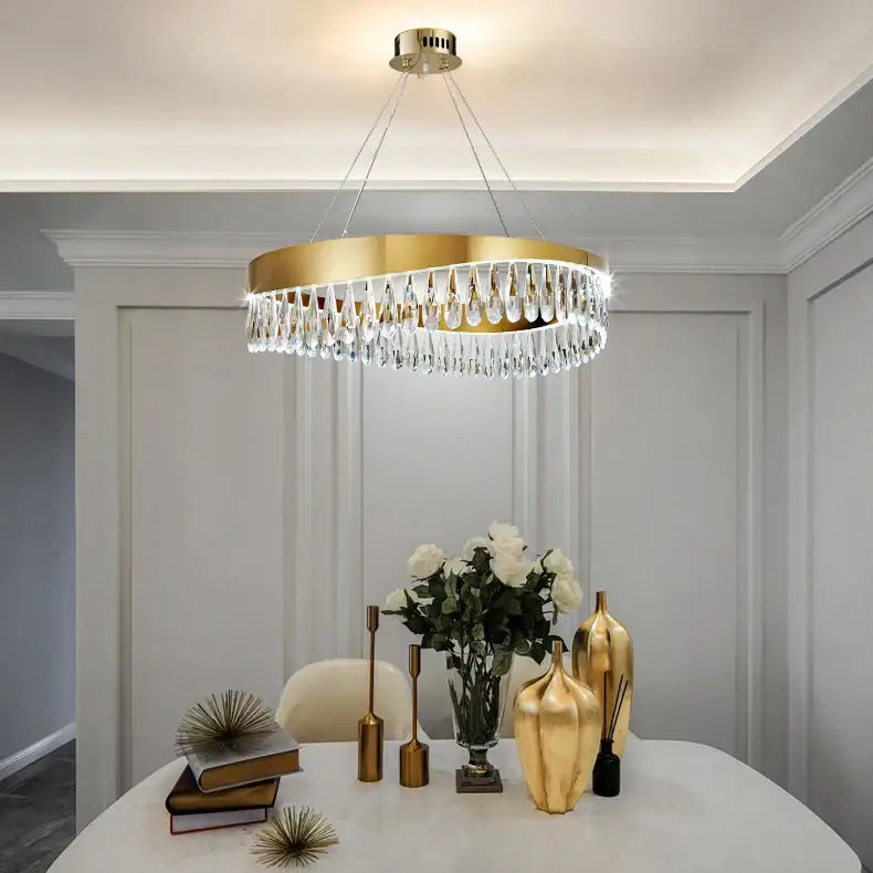 A modern gold-toned circular decorbites crystal stainless steel chandelier with dangling teardrop crystals for foyer decor