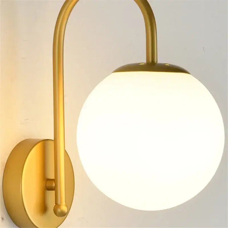 Gold-toned wall sconce with curved metal arm and frosted glass ball led shade for bedroom decorbites glass ball lighting